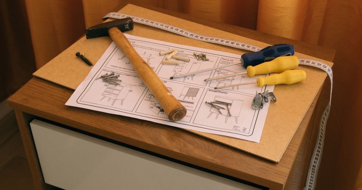 Möbelanleitung, Hammer, Maßband, Schrauben und Schraubendreher auf einem Nachtkästchen